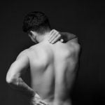 Young man suffering from back pain on black background.