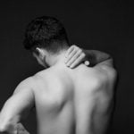 Neck Pain FB featured image Young man suffering from back pain on black background. Health care concept